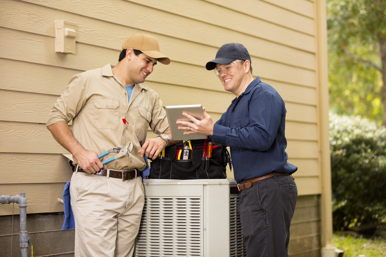 Air conditioner repairmen work on home unit. Blue collar workers.