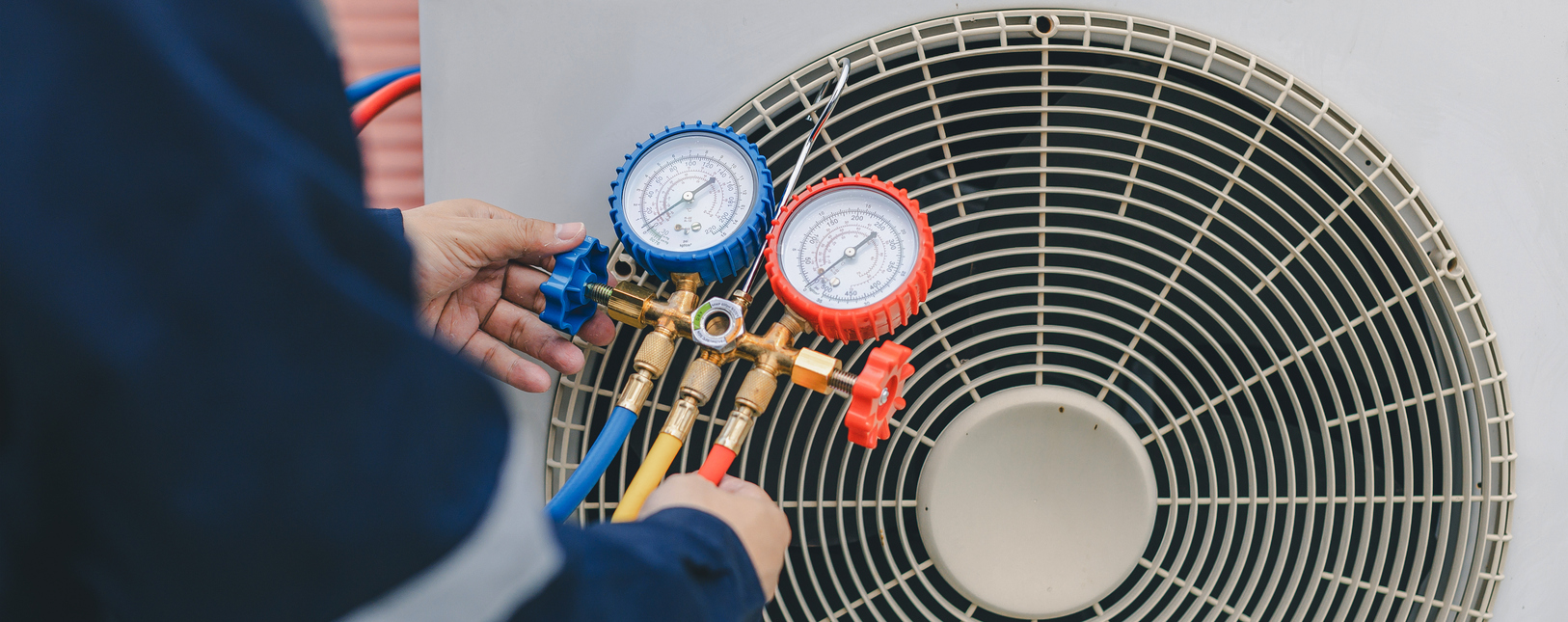 commercial HVAC system design A technician uses a pressure gauge manifold with blue and red dials to check or service an air conditioning units outdoor compressor.